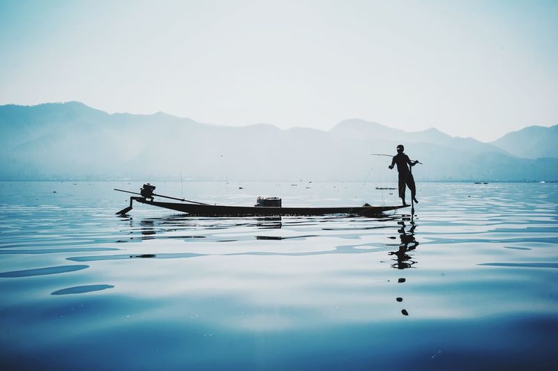 Man fishing in lake against clear sky