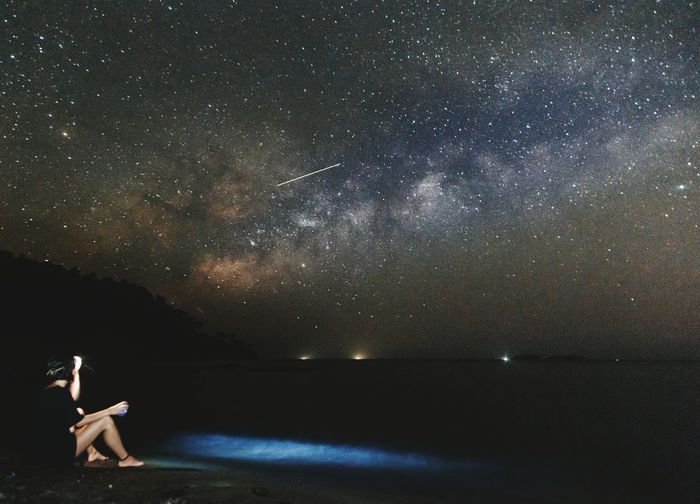 Full length of woman sitting at beach against star field at night