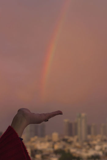 Close-up of hand against rainbow in sky
