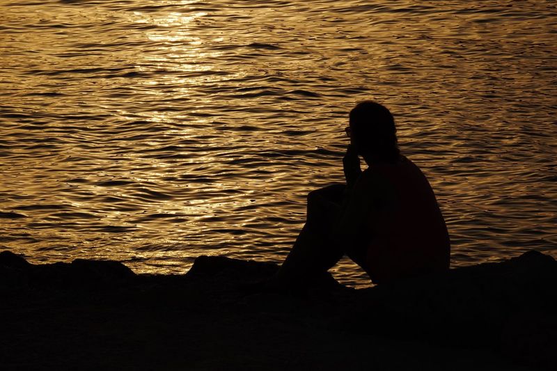 Silhouette woman sitting by sea during sunset