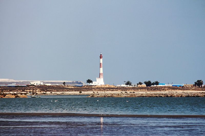 Lighthouse by sea against clear sky