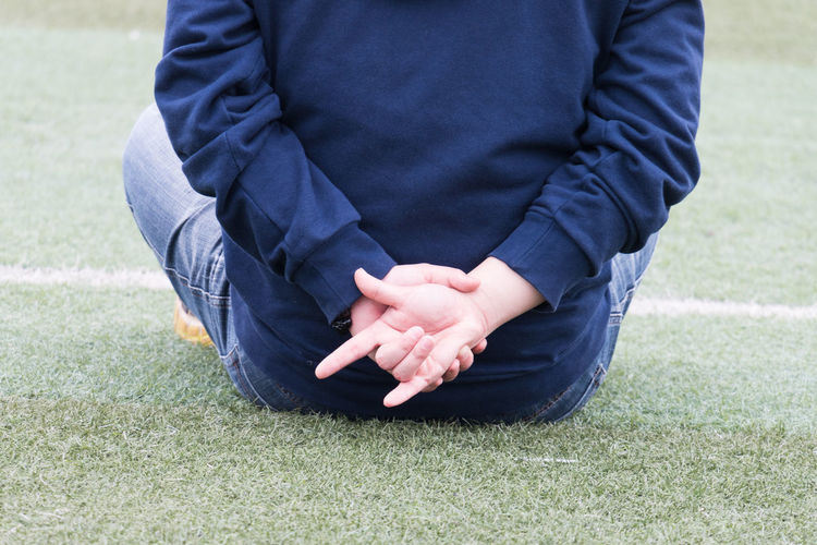 Rear view of man showing horn sign while sitting on field