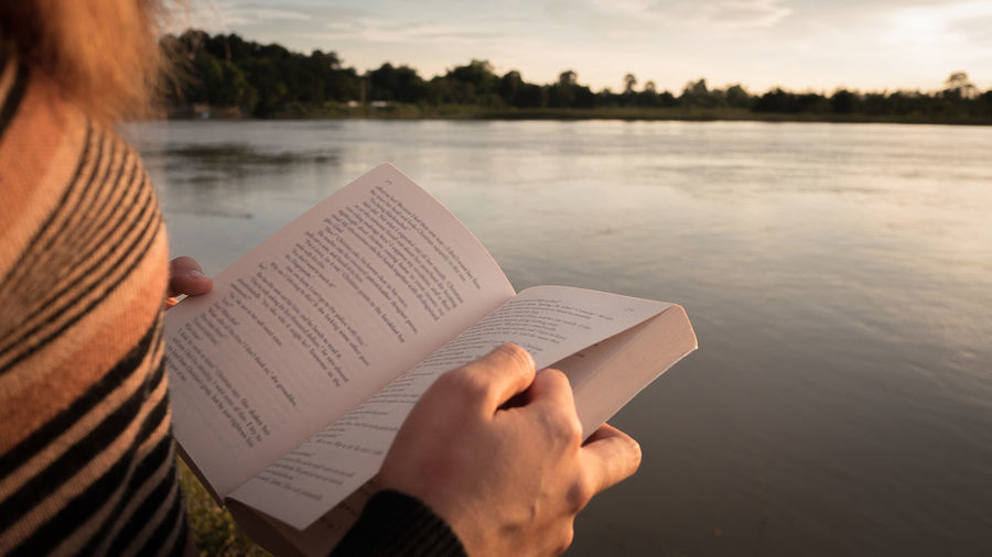 Midsection of woman reading book against lake