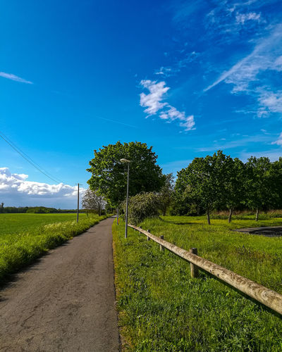Empty road amidst field against sky