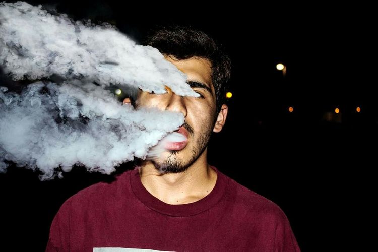 Digital composite image of man exhaling smoke from eyes and nose at night