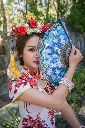 Portrait of young woman wearing qipao holding hand fan