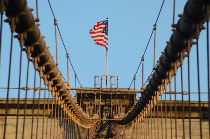 The united states flag on top of brooklyn bridge.