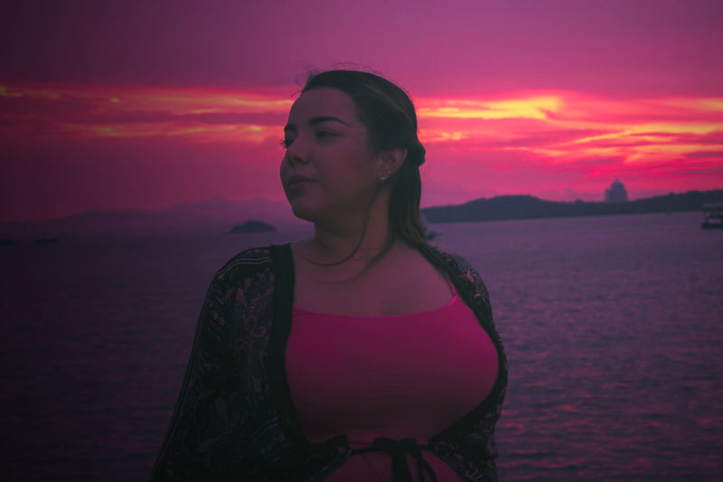 Young woman looking at sea against sky during sunset