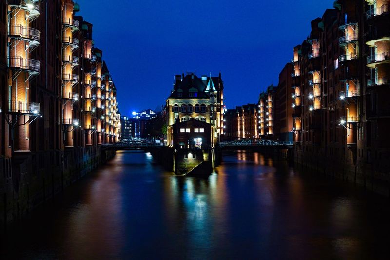 Illuminated canal amidst buildings against sky at night