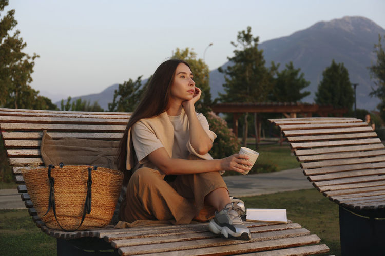 Thoughtful woman with coffee cup sitting on deck chair
