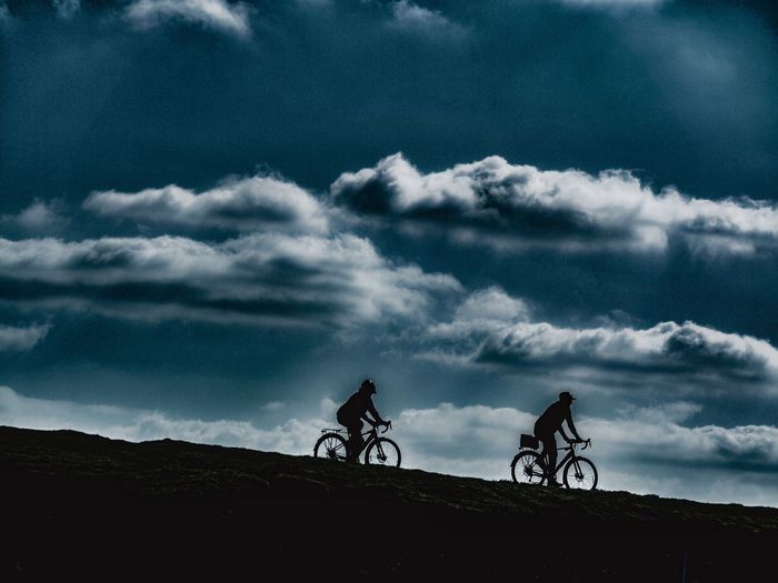 Silhouette people riding bicycle against sky