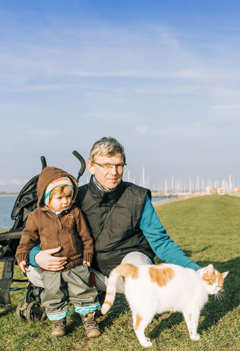 Grandfather and daughter with cat by lake against sky