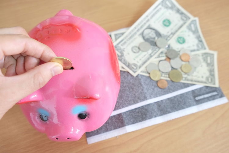 Close-up of hand putting coin in piggy bank on table