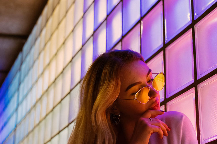 Young woman in sunglasses by illuminated wall