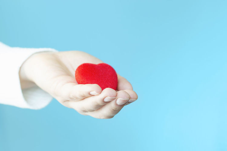 Close-up of hand holding heart shape against blue background