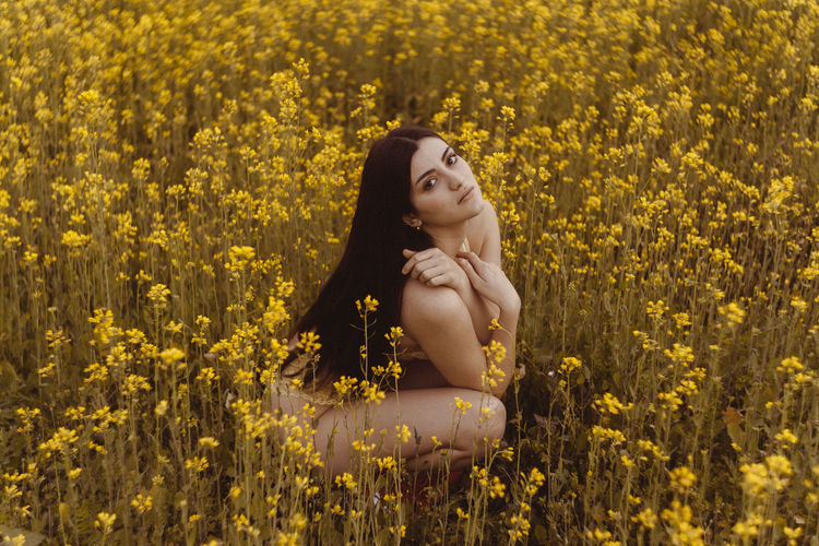 High angle portrait of young woman in bikini sitting amidst flowers on field