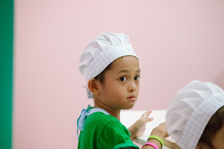 Close-up of cute boy wearing chef hat looking away against wall