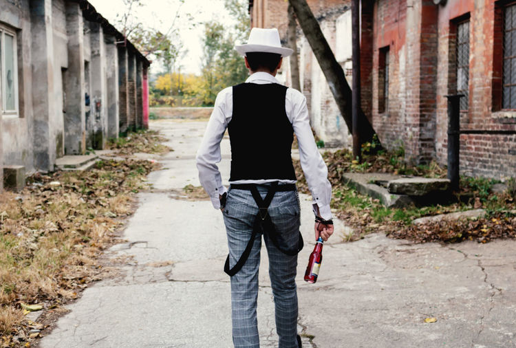 Rear view of retro-styled man carrying beer bottle while walking on the street.