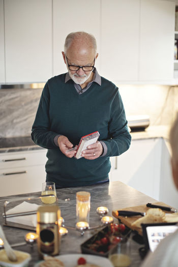 Senior man taking pills while standing by kitchen island at home