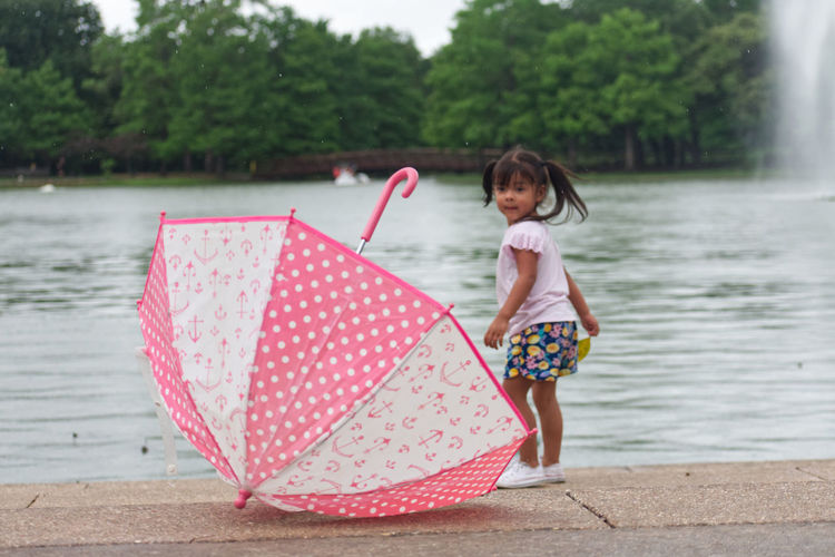 Full length of cute girl with pink umbrella on water