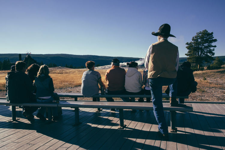 Rear view of people sitting on bench at yellowstone national park against clear sky