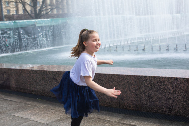 Happy little cute girl having fun in splashes a fountain