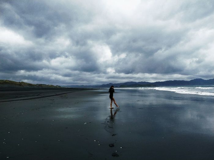 Side view of young woman walking at beach against cloudy sky