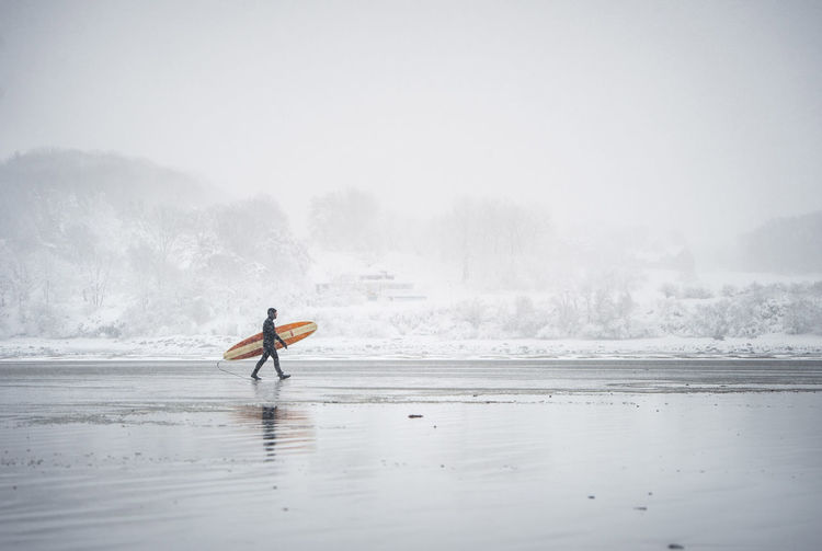 Surfer walking along the beach in maine during a winter snow storm