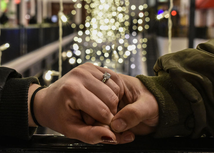 Cropped image of couple holding hands against illuminated lights at night