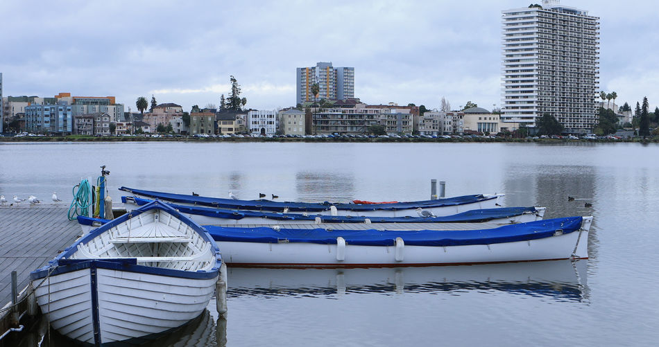 Boats moored on river by buildings against sky