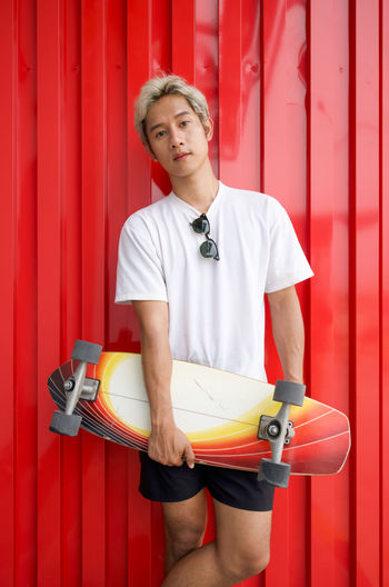 Portrait of man with skateboard standing against red wall