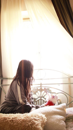 Side view of woman with dog sitting on bed at home