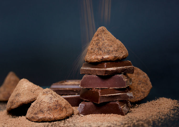Chocolate candy truffle and chocolate pieces and flying cocoa powder on a dark background