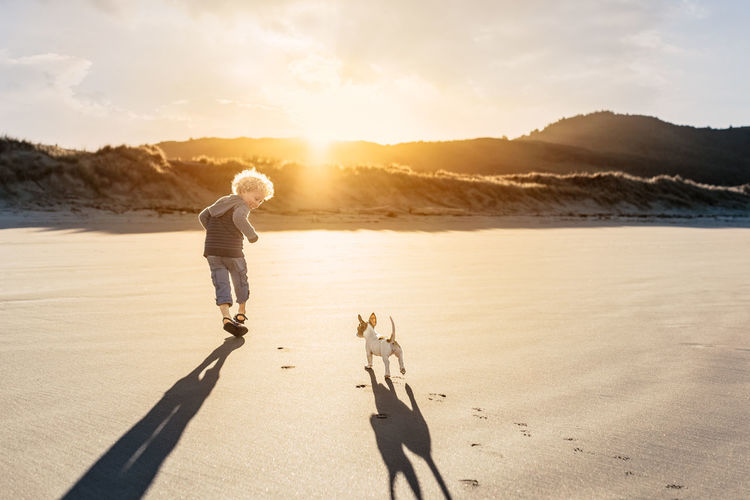 Child and puppy running on a beach together at sunset