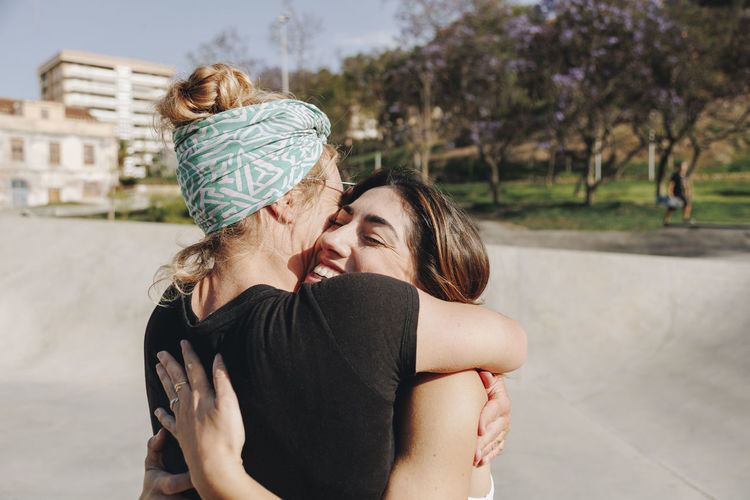 Happy woman embracing friend at skateboard park on sunny day