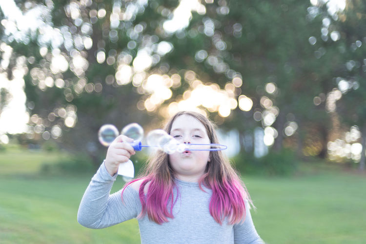 Portrait of girl blowing bubbles in park