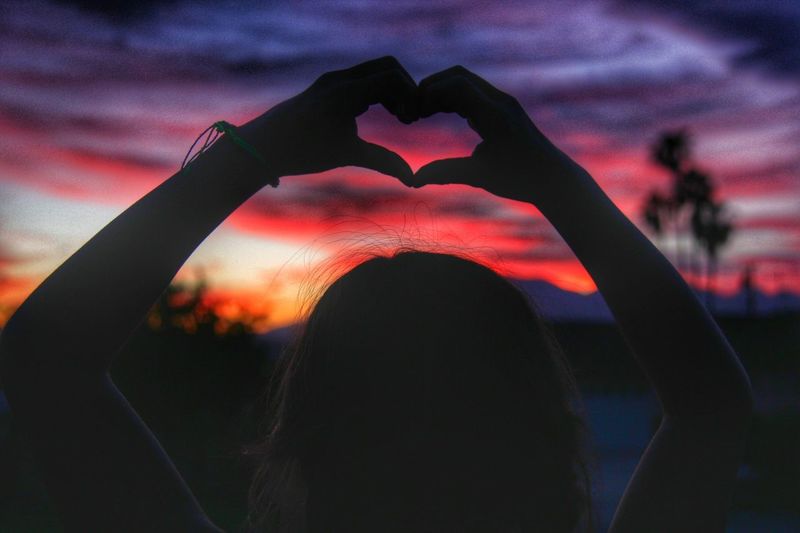 Rear view of silhouette woman making heart shape with hand during sunset