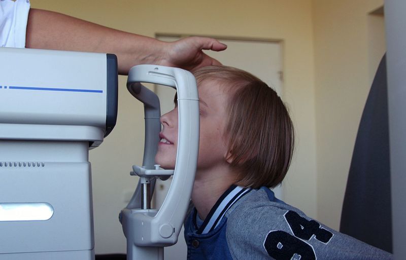 Boy with ophthalmologist looking through refractometer at clinic