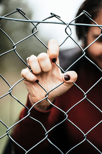 Hand of a woman in red sweater with dark manicured nails pushing against rustical metal fence. 