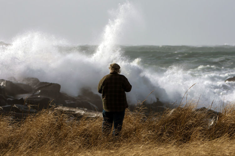Rear view of man standing against splashing waves