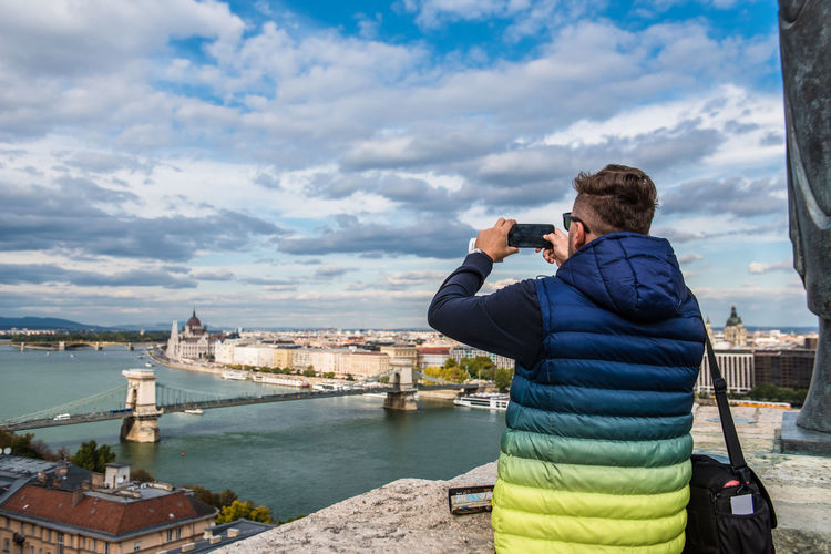 Rear view of man photographing cityscape against sky