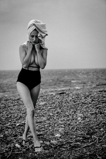 Full length of seductive woman walking at beach against sky