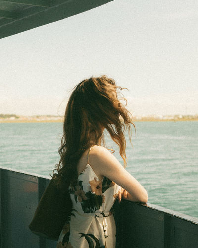 Side view of woman looking at sea while standing by railing