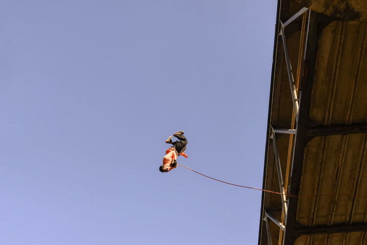 Low angle view of man jumping against clear sky