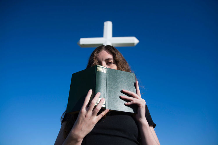 Low angle view of woman reading book against blue sky