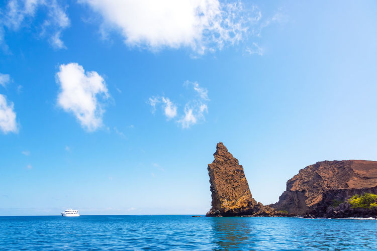 Scenic view of yacht at sea and rock formations against blue sky
