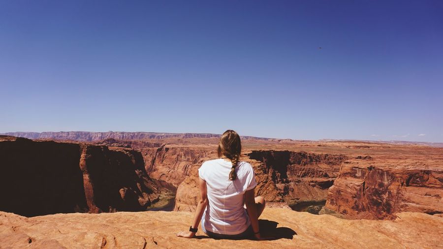 Rear view of woman sitting on rock formation at horseshoe bend against clear sky