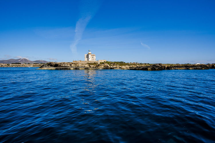 Lighthouse on building by sea against blue sky