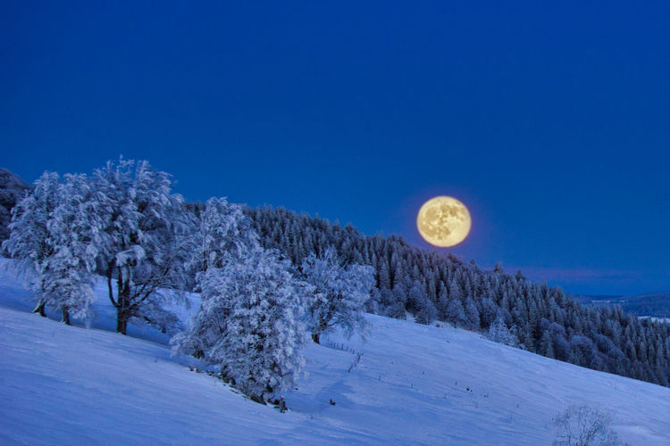 Scenic view of snow covered land against clear blue sky with full moon