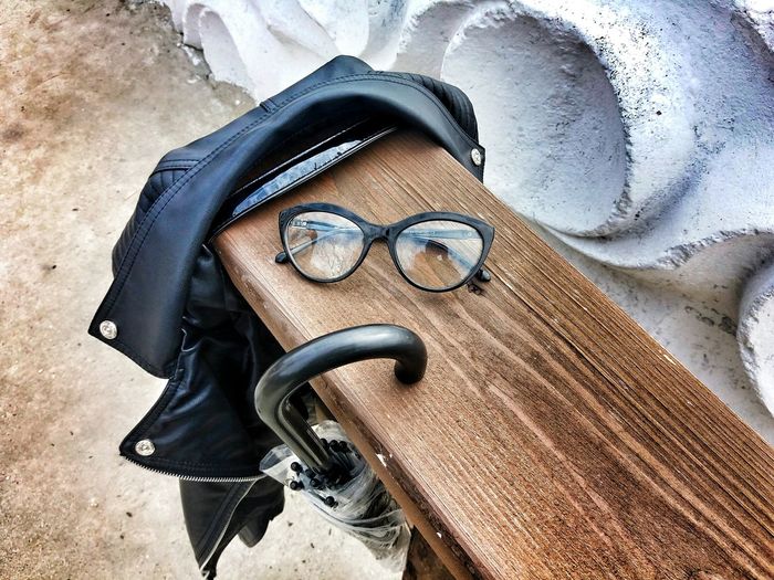 High angle view of eyeglasses with leather jacket and umbrella on wooden bench